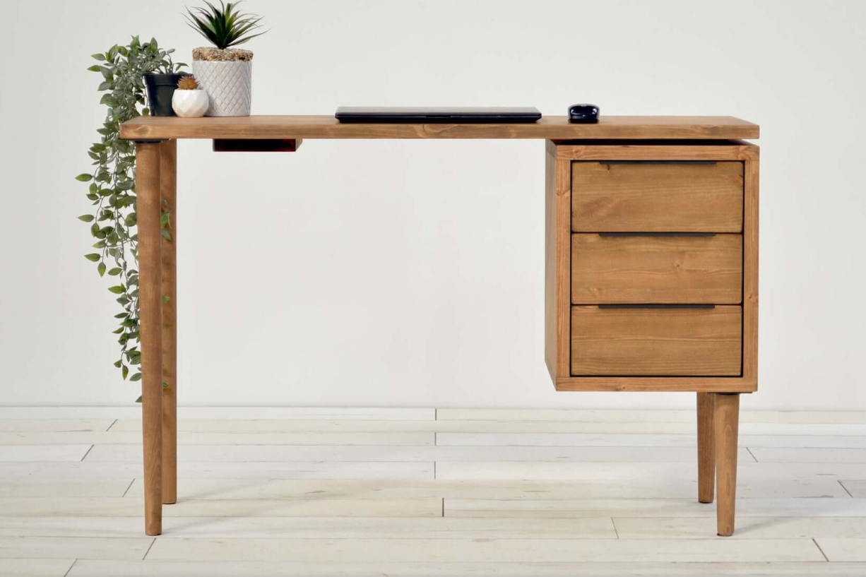 A mid-century executive desk with a drawer pedestal, made of wood, displayed in a medium oak color. The image shows the desk with a potted plant on top and the brand name 'Harvey' at the bottom.